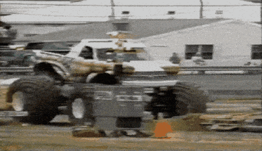a monster truck is driving down a dirt road next to a trash can that says ' gm ' on it
