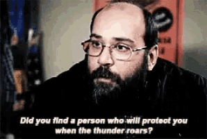 a bald man with glasses and a beard is talking to someone .