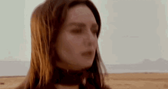 a close up of a woman 's face in the desert with mountains in the background .