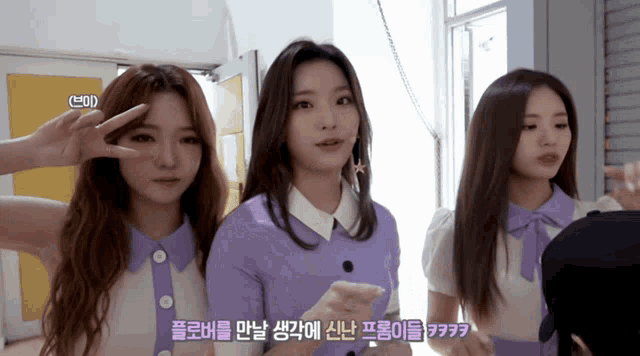 three girls are standing next to each other and one of them is wearing a purple sweater