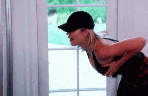 a woman wearing a baseball cap and bra is standing in front of a door .