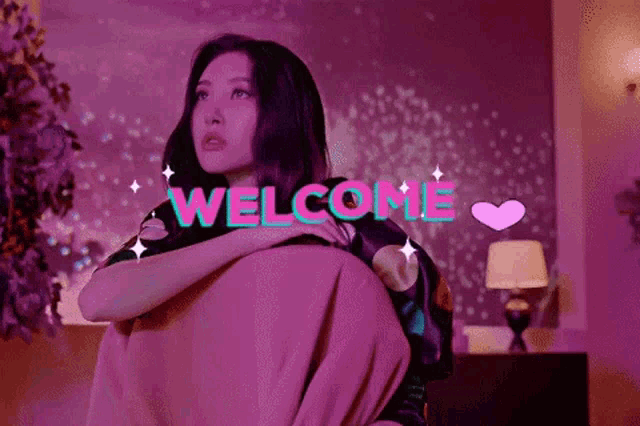 a woman is sitting on a couch in a room with the words welcome written on the screen behind her .