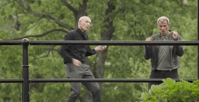 two men are standing next to each other on a fence .