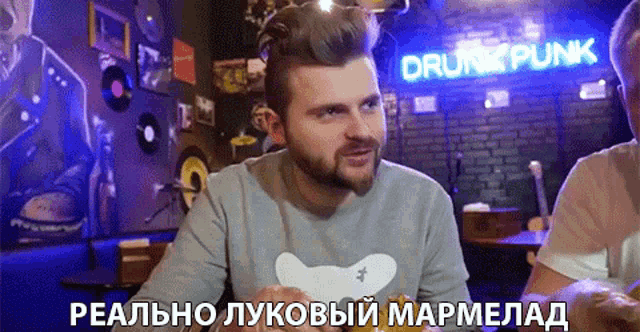 a man in a grey shirt is sitting in front of a neon sign that says drunk punk
