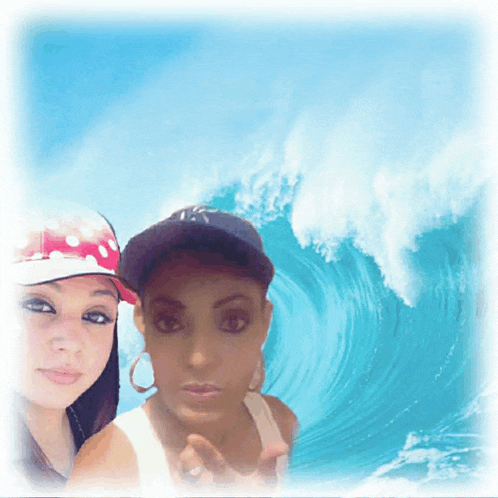 two women are posing for a picture in front of a large wave