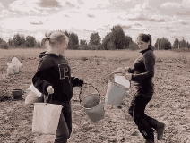 two women carrying buckets in a field with one wearing a sweatshirt that says le