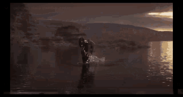 a man is doing a trick on a motorcycle in the water with a skull and crossbones logo in the corner