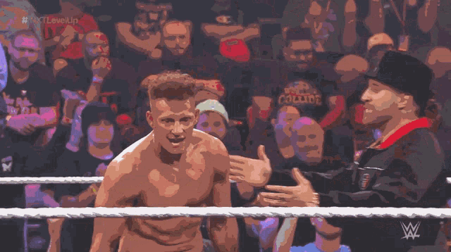 a man in a wrestling ring is talking to another man in front of a crowd with the words # nxt level up visible