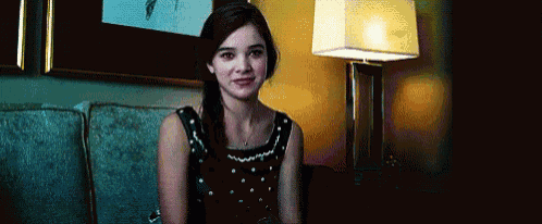 a woman in a black dress is sitting on a couch in front of a lamp and smiling .