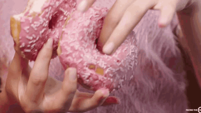 a woman is holding a pink donut in her hands