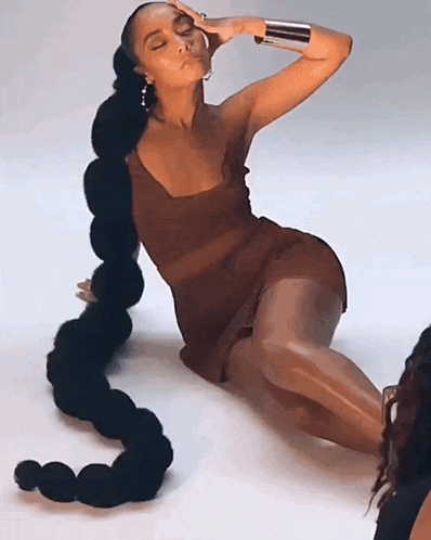 a woman in a brown dress with a very long ponytail is sitting on the floor .