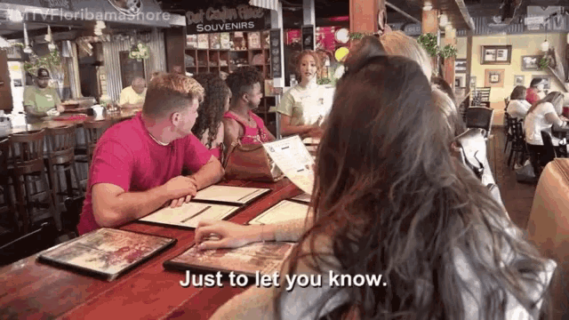 a group of people are sitting at a table in a restaurant with a sign that says just to let you know