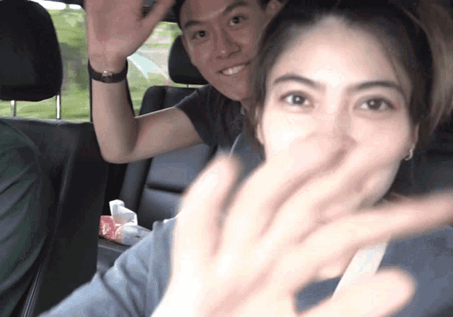 a man and a woman are sitting in a car and the woman is waving