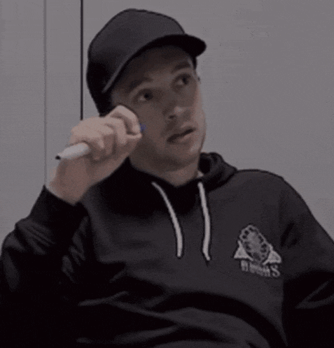a man wearing a hat and a black hoodie is talking on a cell phone .