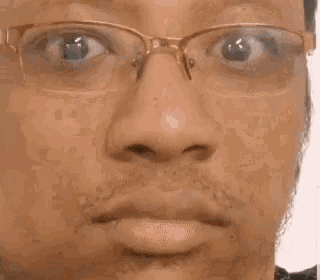 a man with a beard and glasses is leaning against a wall and making a funny face .