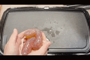 a person is holding a piece of meat in their hands over a grill .