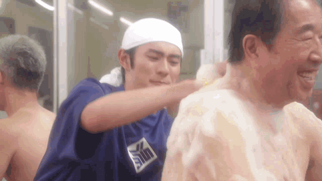 a man is washing another man 's back with a shirt that says sin