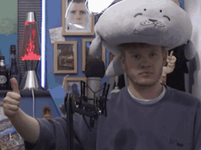 a man wearing a stuffed seal hat gives a thumbs up
