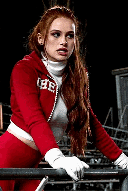 a woman wearing a red jacket and white gloves is leaning on a railing .