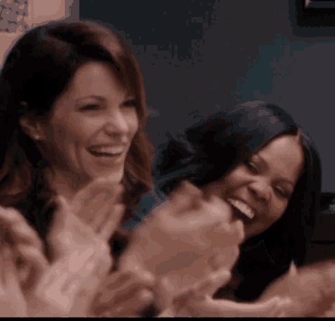 two women are laughing and clapping their hands in a crowd of people .
