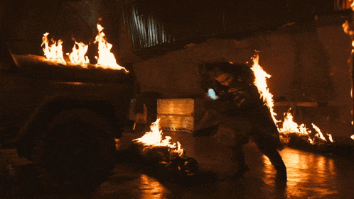 a man is laying on the ground in front of a car on fire