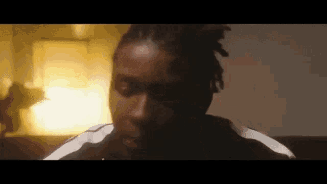 a man with dreadlocks is sitting on a couch in a dark room looking at the camera .