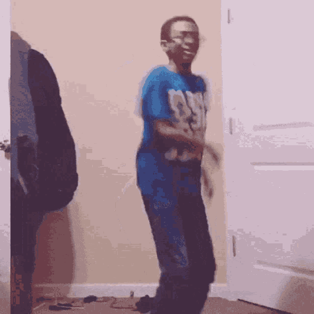 a boy in a blue shirt with the word cowboys on it is dancing in a room