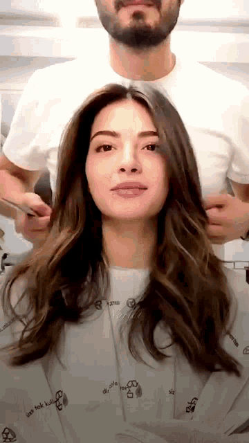a woman is getting her hair cut by a man wearing a white shirt that says ' use tek kull ' on it