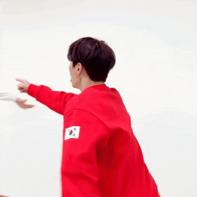 two men are standing next to each other in front of a white wall . one of the men is wearing a red sweatshirt .