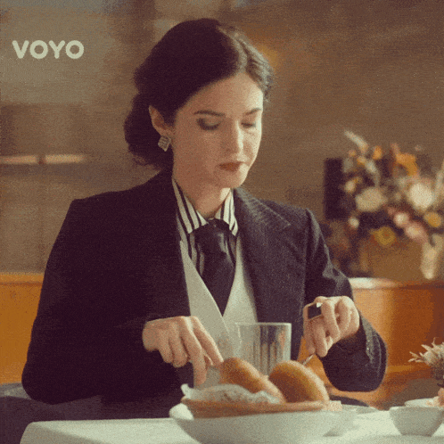 a woman in a suit sits at a table with a bowl of bread and a sign that says voyo