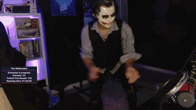 a man wearing a joker mask sits in front of a screen that says " the riftbreaker "