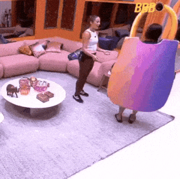 two women are standing in a living room next to a couch and a table .