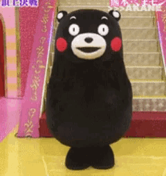 a black teddy bear costume is standing on a yellow floor in front of stairs .