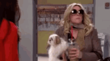 a woman is holding a small dog in her arms and drinking from a cup .