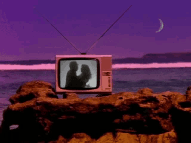 a television with a couple kissing on the screen is sitting on a rock near the ocean