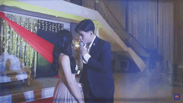 a man in a suit is singing into a microphone to a woman in a dress .