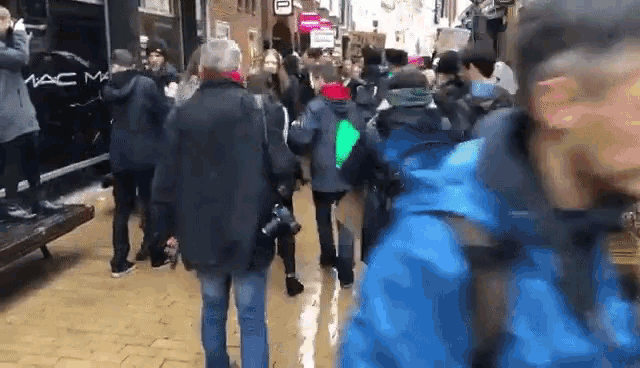 a crowd of people are walking down a street in front of a mac makeup store