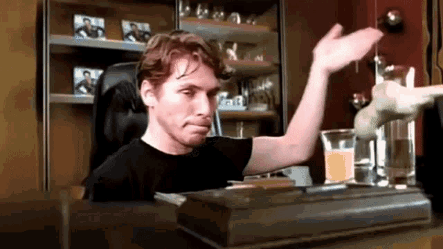 a man in a black shirt is sitting at a table with a glass of orange juice