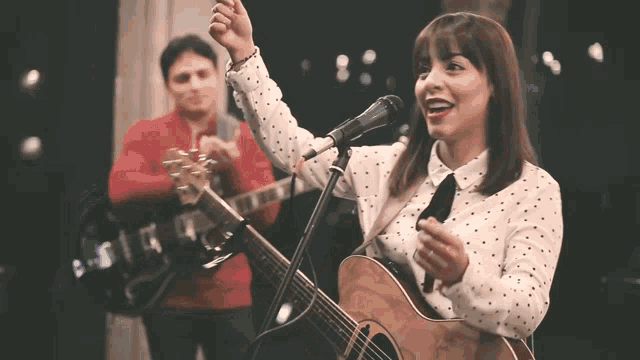 a woman singing into a microphone while a man plays a guitar in the background