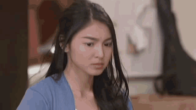a woman in a blue sweater is making a funny face and looking at the camera .