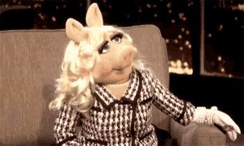 miss piggy is sitting on a couch wearing a suit and gloves .