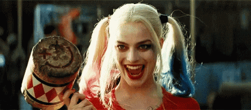 harley quinn from suicide squad is holding a drum with a smiley face on it and smiling .
