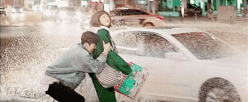 a man is carrying a woman in the rain while a car is driving by .