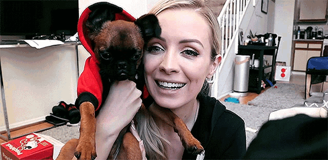 a woman is holding a brown dog in her arms and smiling .