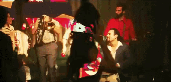 a man in a suit is kneeling down in front of a group of people playing instruments