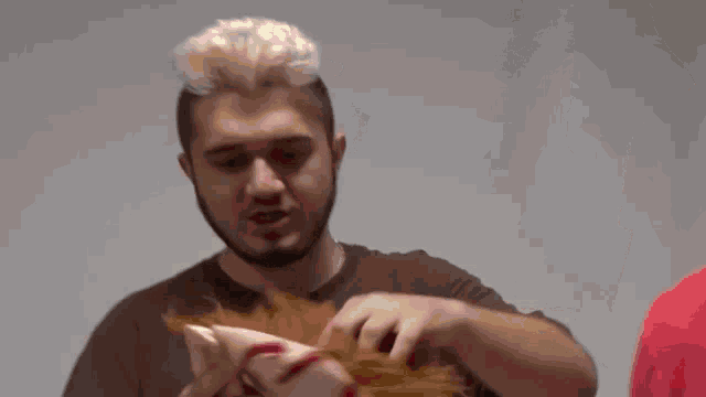 a man in a red shirt is holding a gold mask over his face