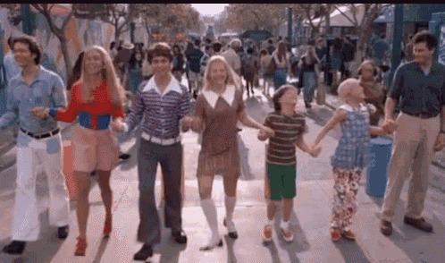 a group of people are holding hands while walking down a sidewalk .