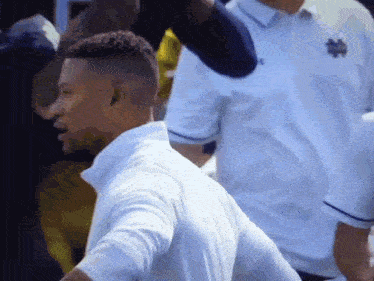 a man in a white shirt with a notre dame logo on it is standing in a crowd .