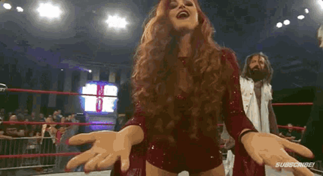 a woman is standing in a wrestling ring with her arms outstretched and a man standing behind her .