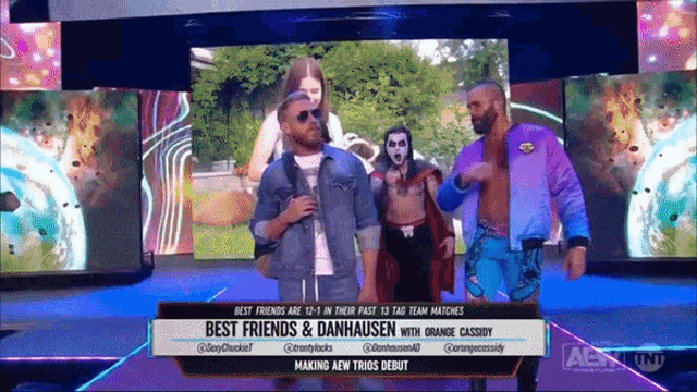 a group of men are standing on a stage with a banner that says best friends & danhausen with orange cassidy